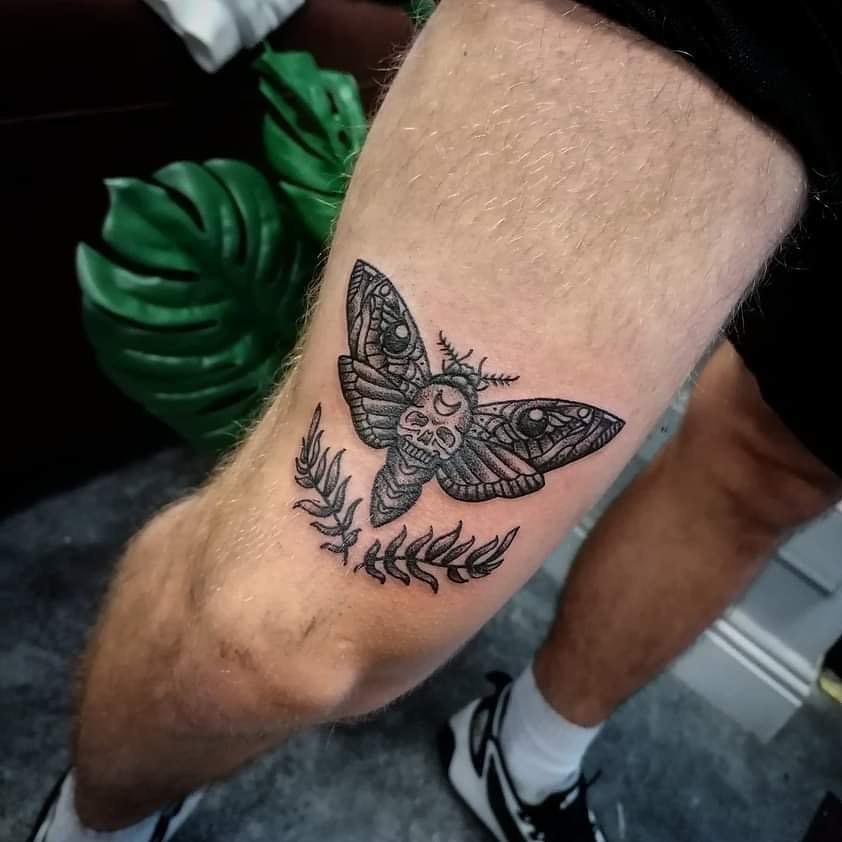 Tatuaje de polilla negra en la rodilla.