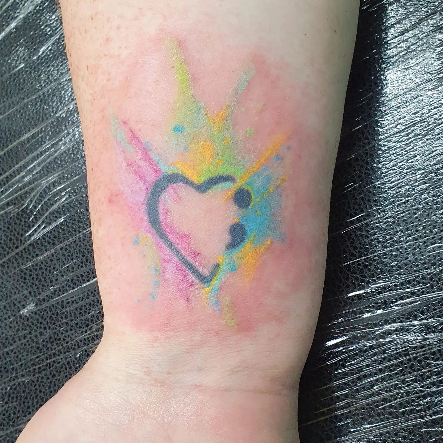 Tatuaje de punto y coma en tono pastel claro.