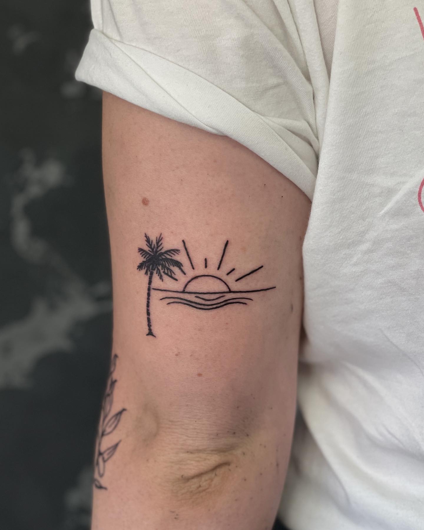 Tatuaje simple de palmera y atardecer en el brazo.