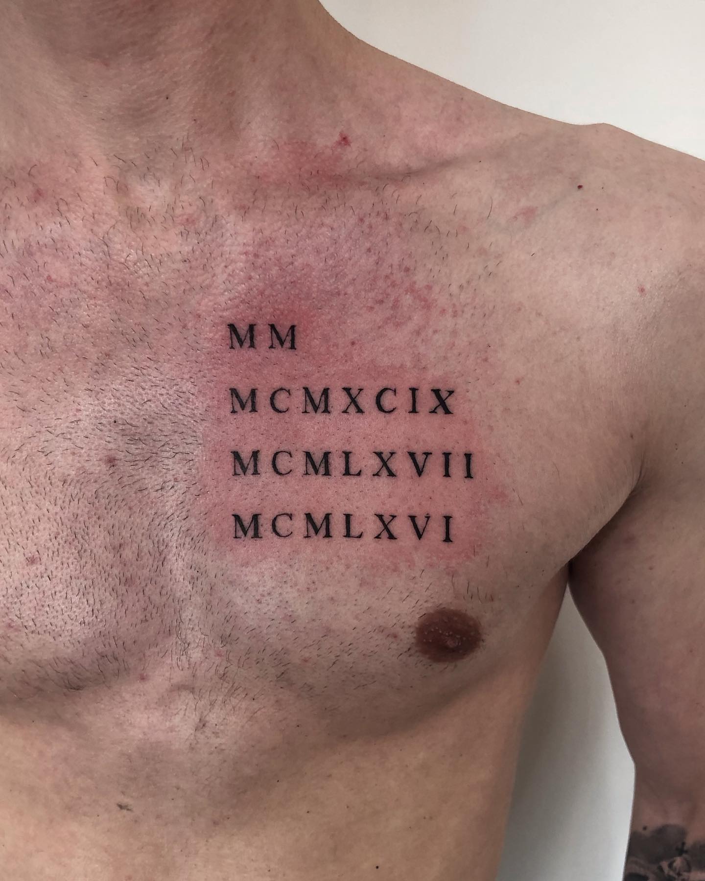 Pequeño tatuaje de número romano en el pecho.