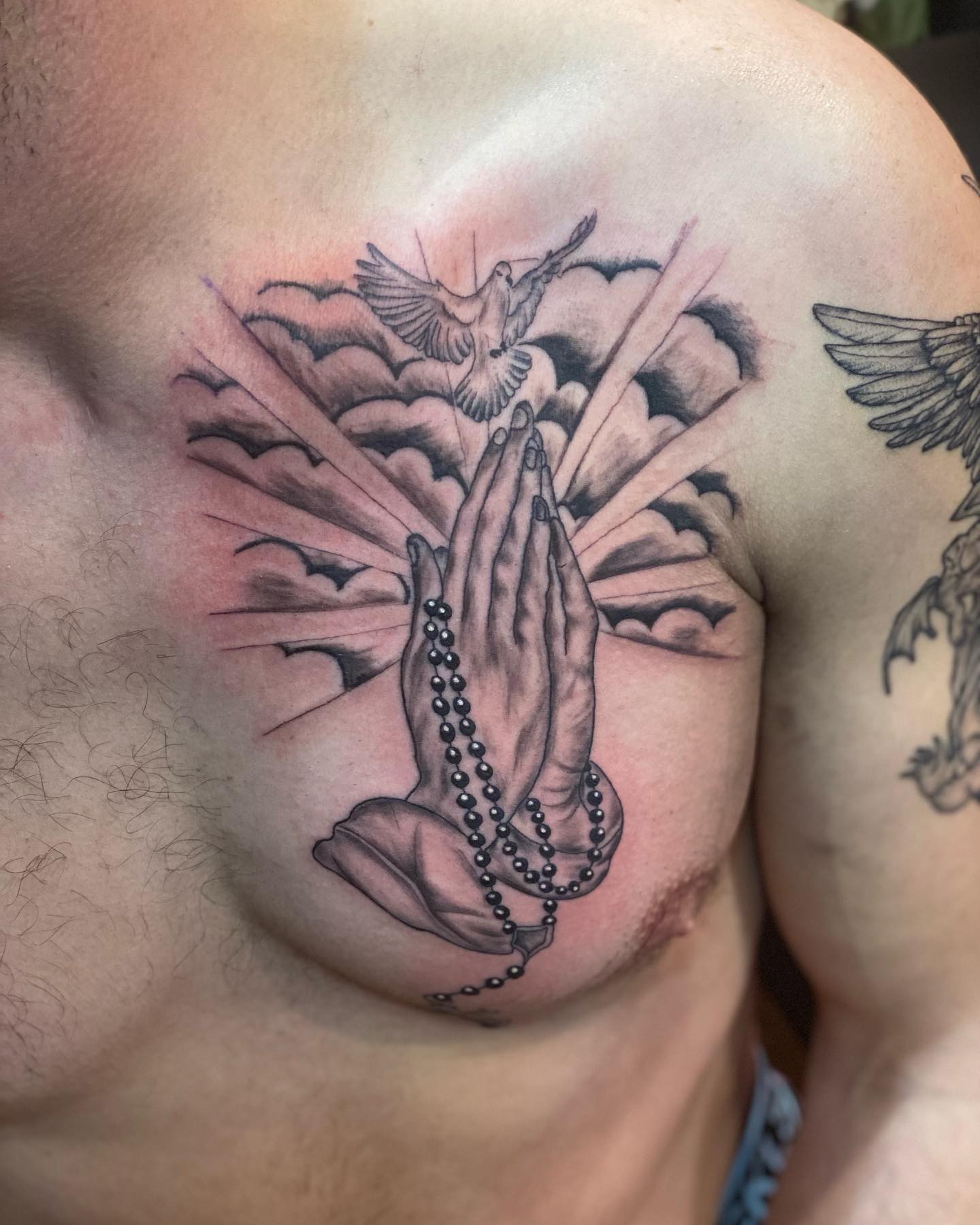 Tatuaje de manos rezando en el pecho.