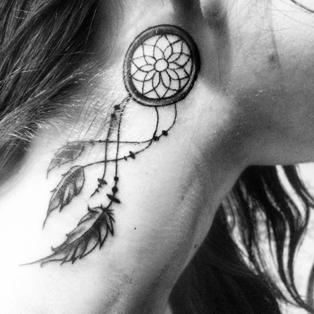 Tatuaje de atrapasueños negro detrás de la oreja.