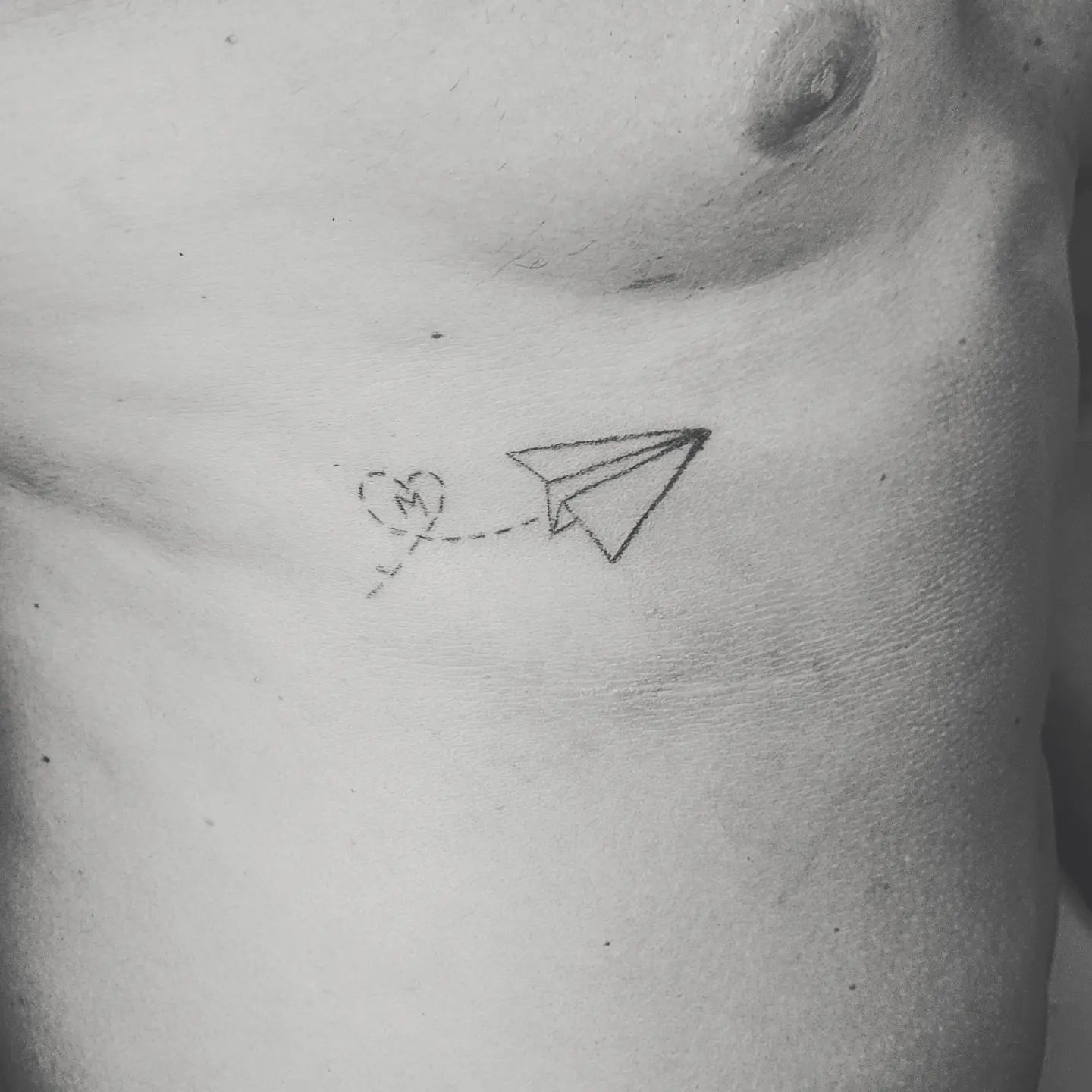 Pequeño tatuaje de avión de papel negro.
