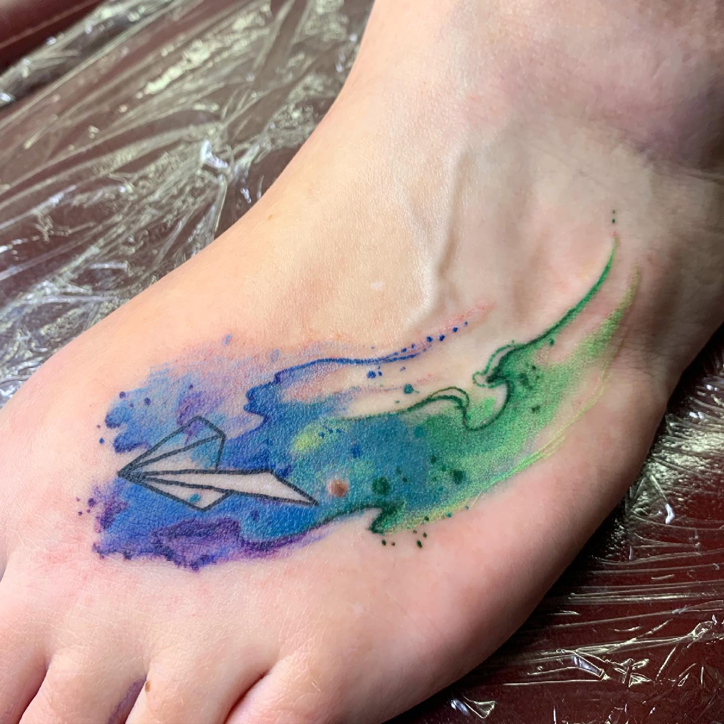 Tatuaje de avión de papel en el brazo.